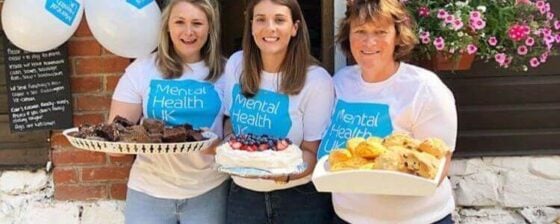 Three women hold cakes on plates with Mental Health UK t-shirts and balloons