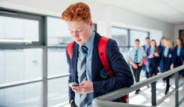 Young boy walking ahead of a group at school looking at his mobile