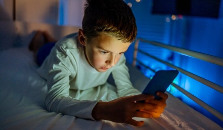 Young boy in bed at night looking at his mobile