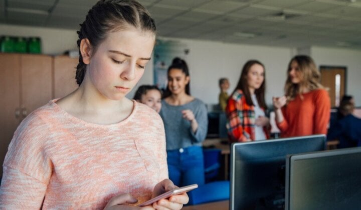 Young girl looking at her mobile with others pointing at her in the background